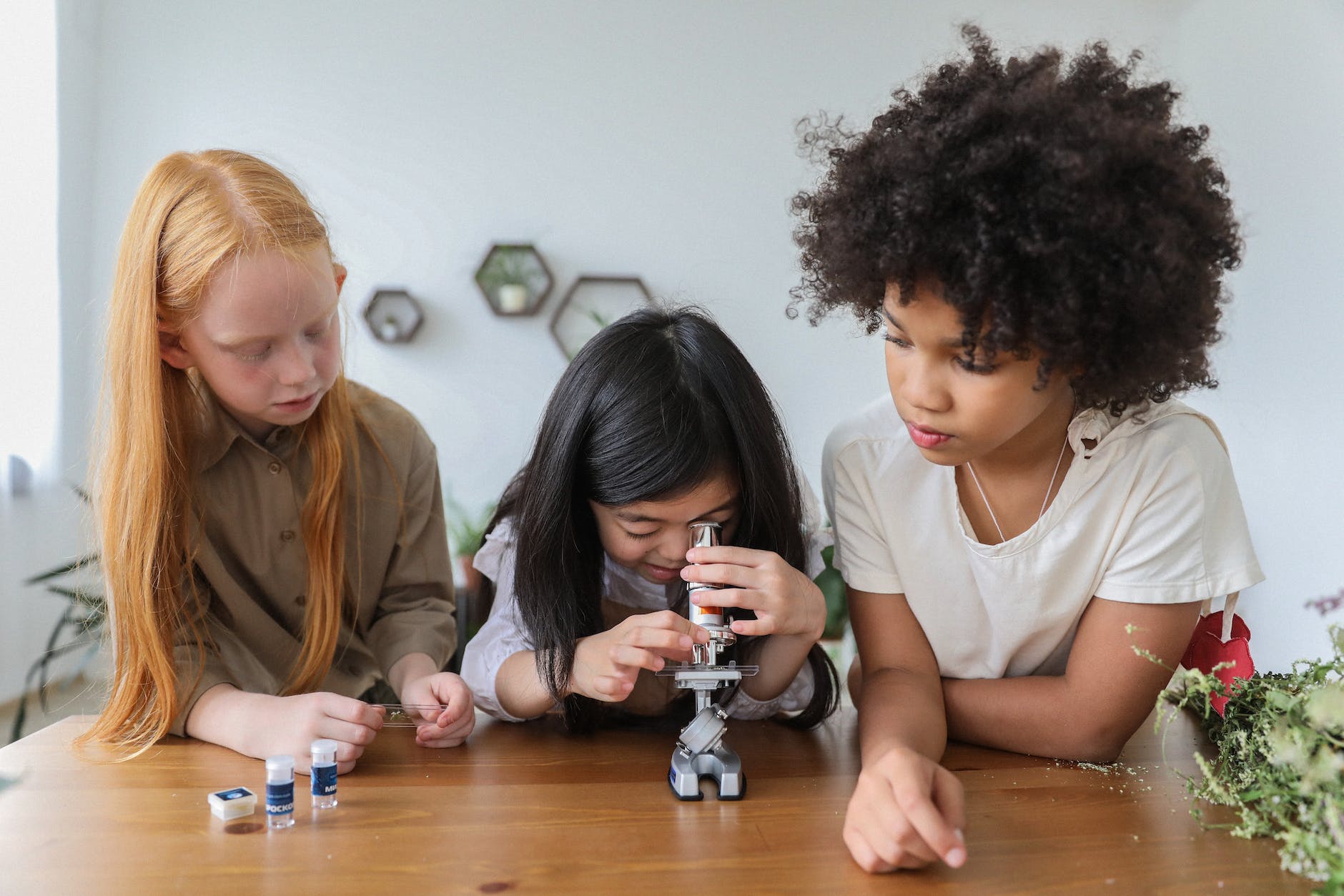 Three girls look through a microscope.